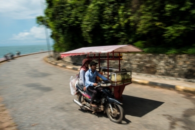 A tuk tuk selling snacks and drinks drives along the coastal road