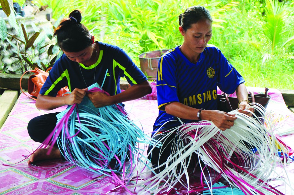 Artisans weaving bags out of colourful plastic straps. Credit: Helping Hands Penan